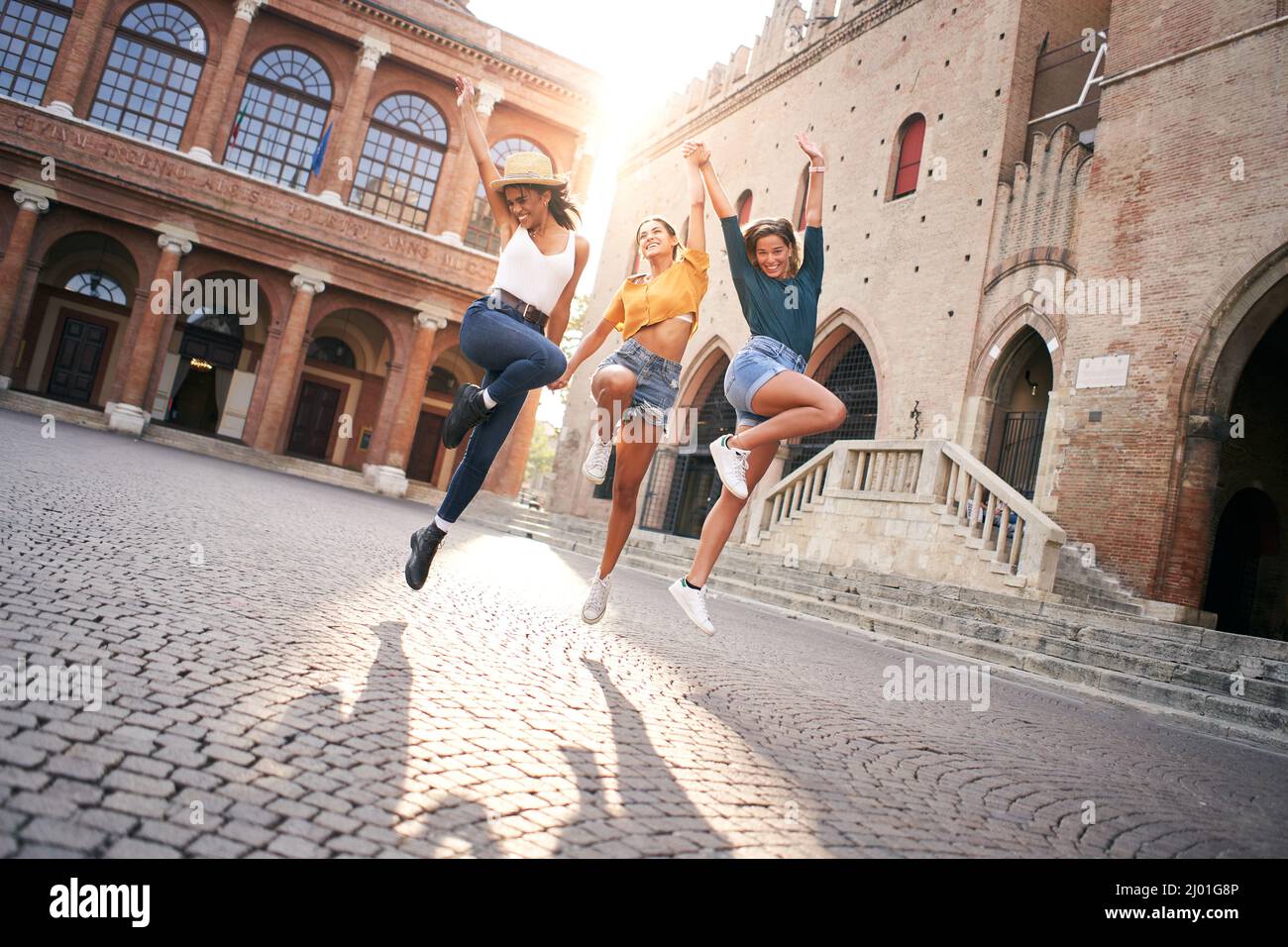 Des femmes heureuses qui s'amusent ensemble à Venise. Trois jeunes femmes sautent en tenant hans, groupe multiracial rire ensemble. Style de vie, liberté, célébration Banque D'Images