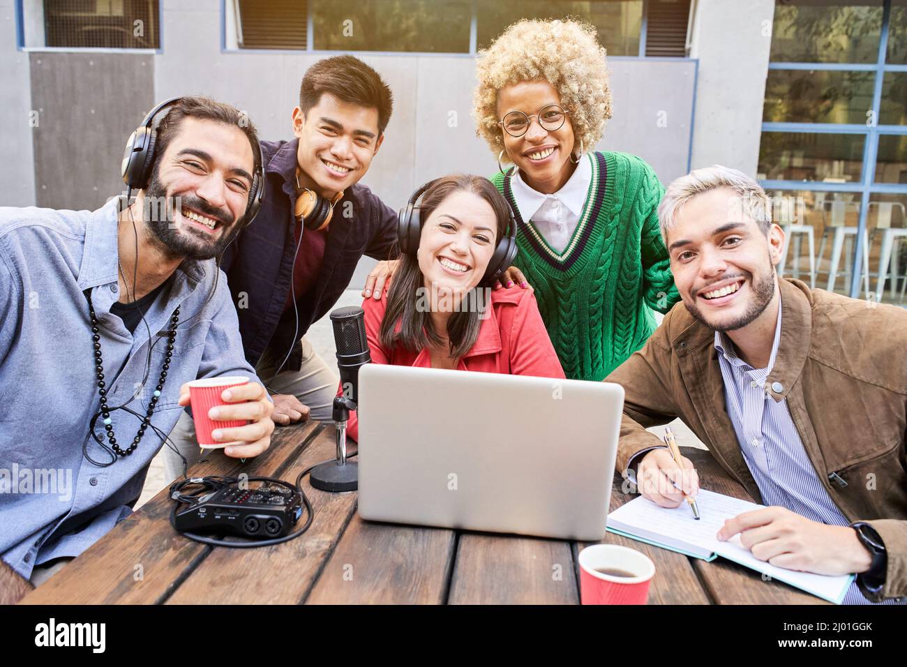 Portrait regardant la caméra d'un groupe de jeunes souriants en plein air regardant une vidéo sur l'ordinateur portable. Collègues qui diffusent des rencontres Banque D'Images