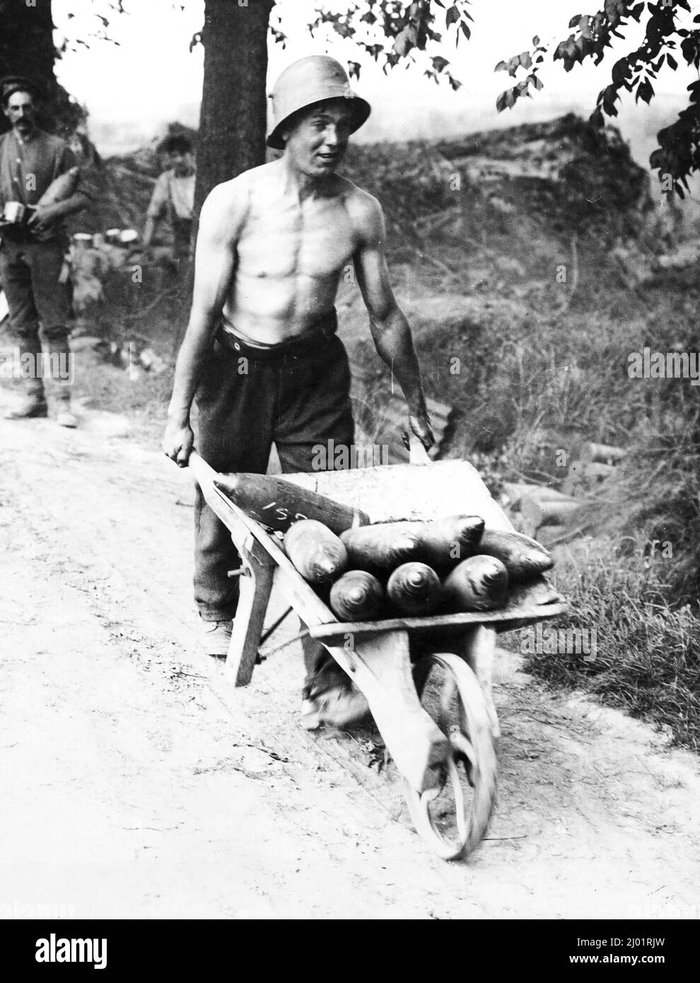 Un jeune soldat portant un casque allemand pousse une brouette pleine de coquillages sur une route poussiéreuse à Messines. Derrière lui se trouvent deux autres soldats, l'un tenant une coquille. Banque D'Images