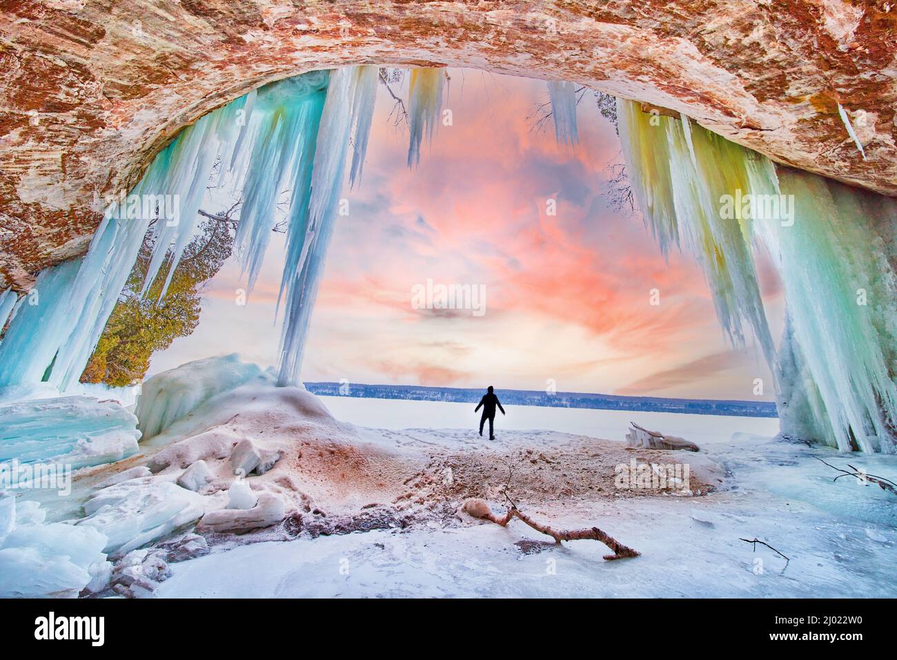 Silhouette humaine à l'entrée de la magnifique grotte de glace au lever du soleil d'hiver avec des glaçons bleus et verts Banque D'Images