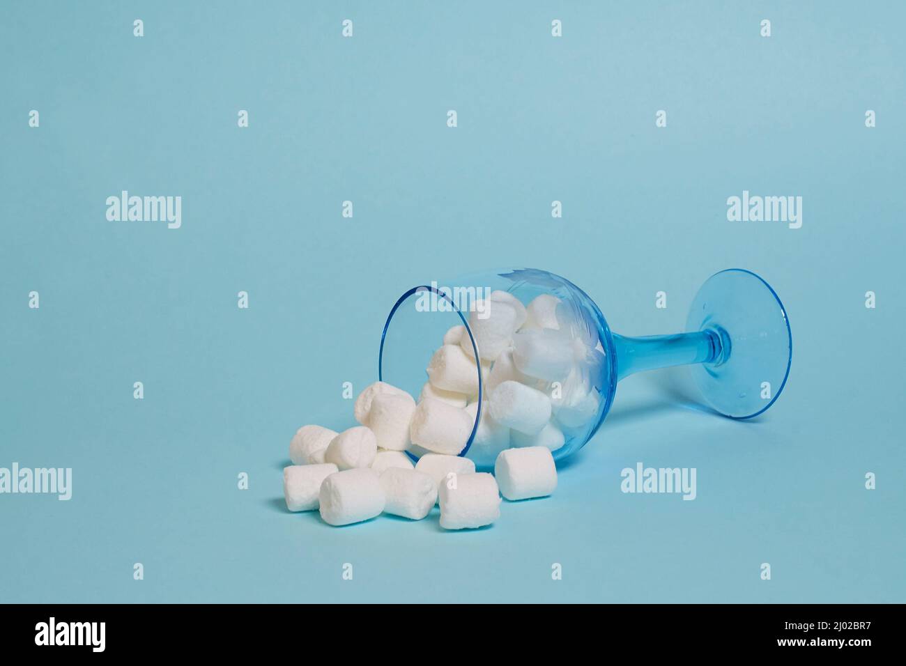 Guimauve blanche dans un verre à vin renversé sur fond bleu Banque D'Images