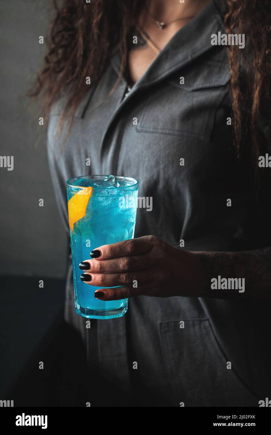 Femme tenant un cocktail bleu dans une balle haute avec de la glace Banque D'Images