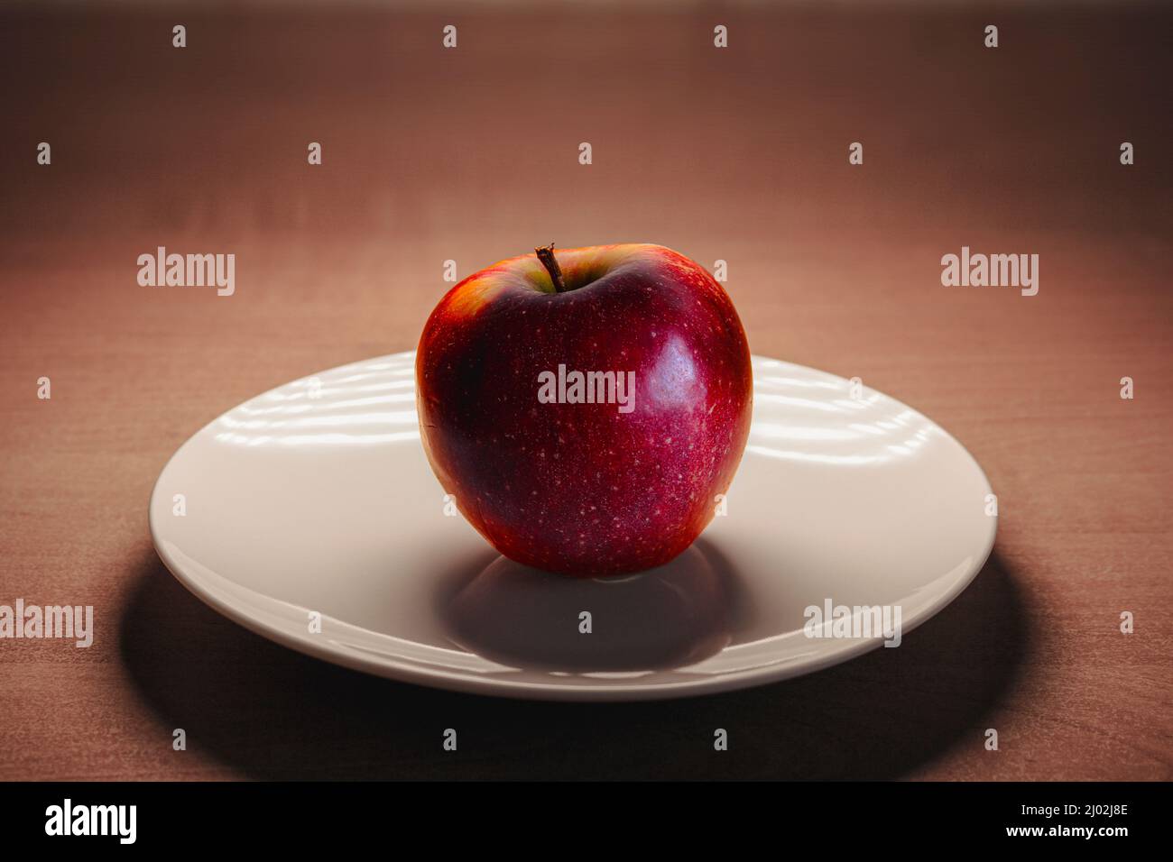 Pomme rouge mûre sur une plaque blanche sur une table en bois. Banque D'Images