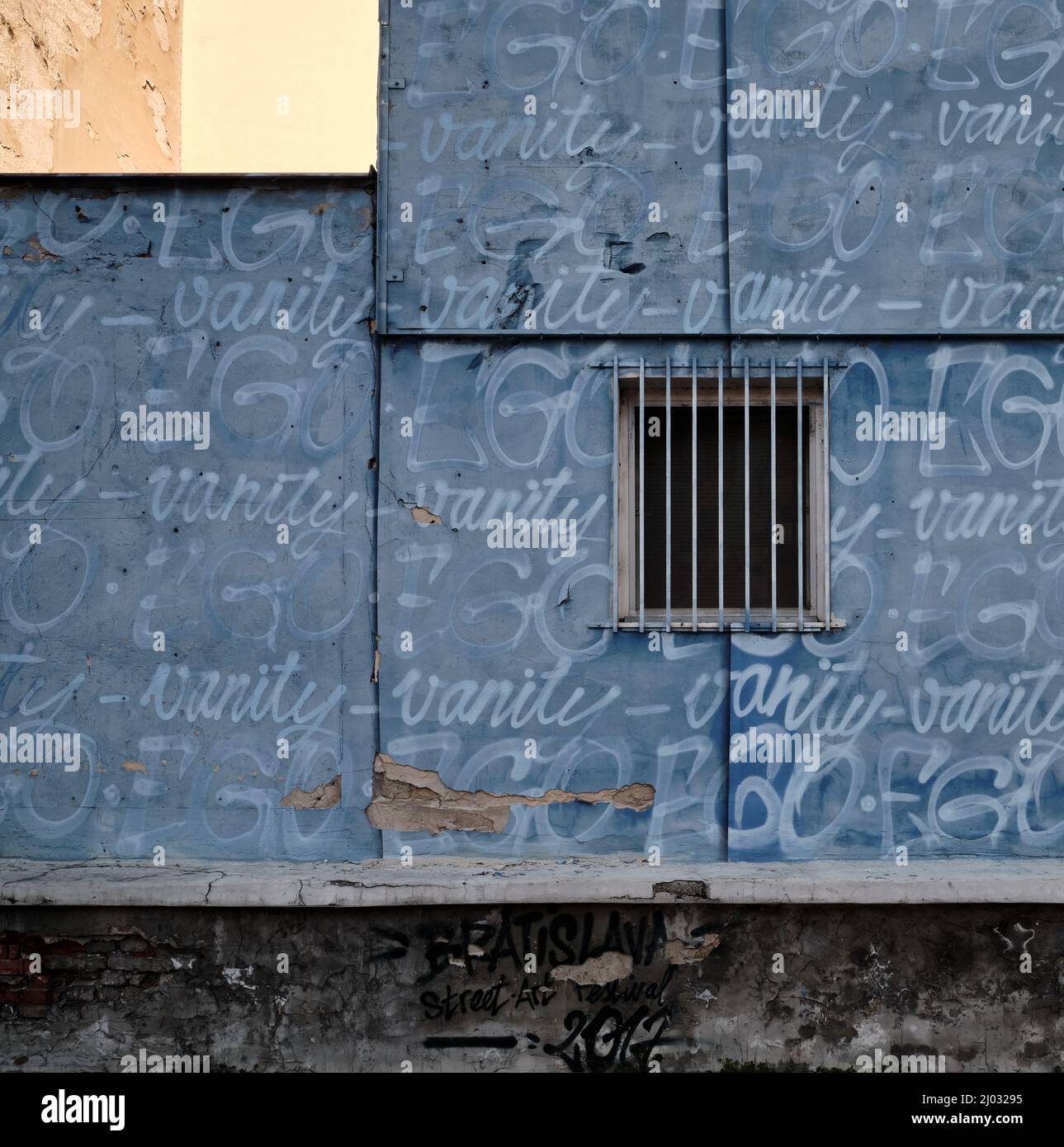 Fenêtre barrée sur une façade couverte de graffitis bleus avec texte répété de vanité à Bratislava, Slovaquie. Banque D'Images