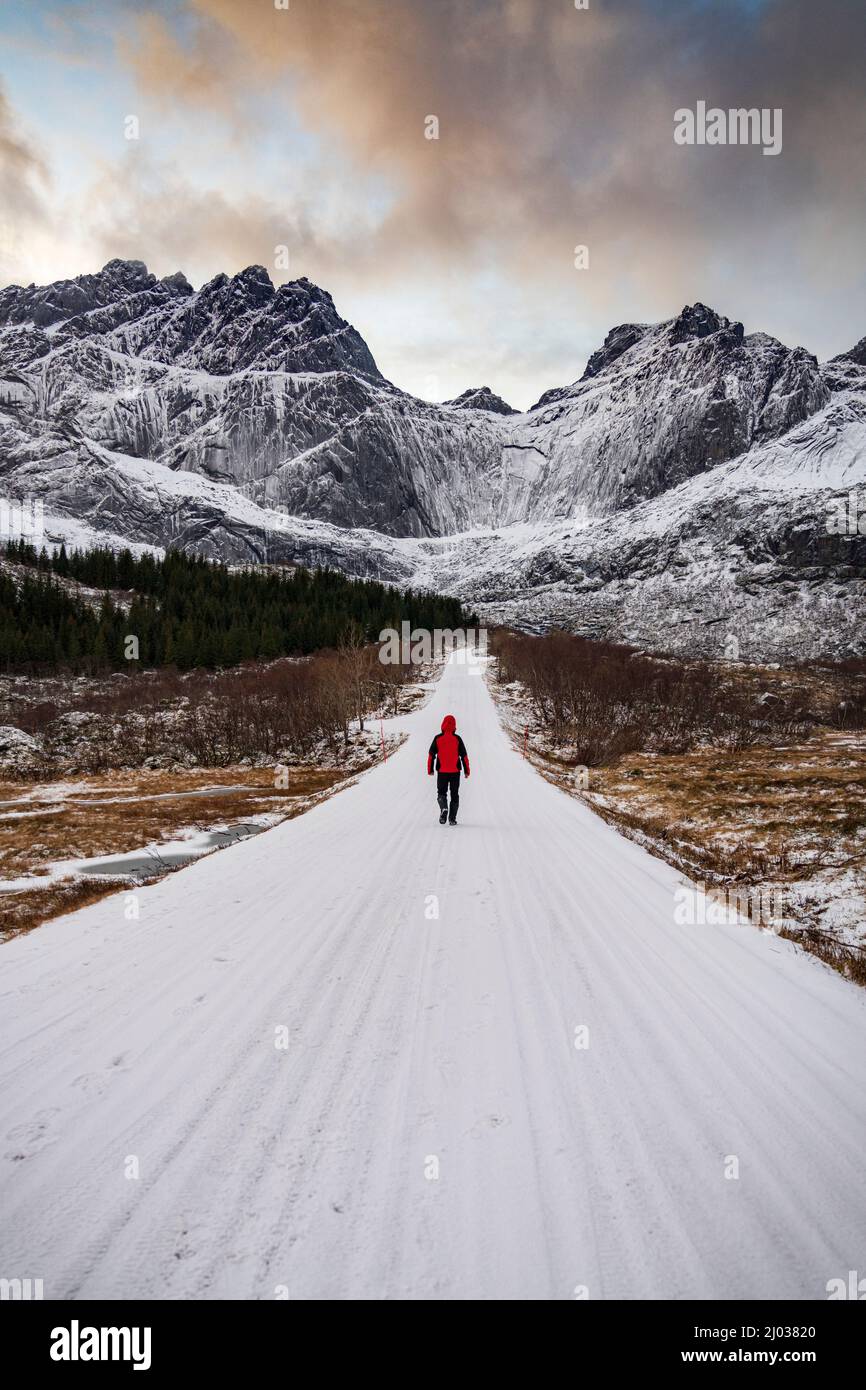 Homme marchant sur une route de montagne vide couverte de neige en hiver, Nusfjord, comté de Nordland, îles Lofoten, Norvège, Scandinavie, Europe Banque D'Images