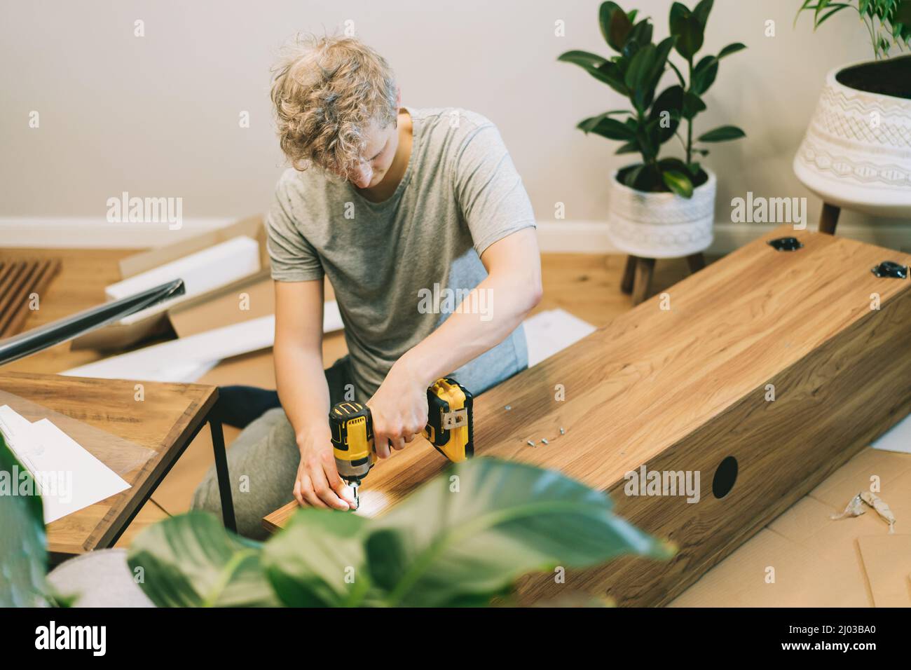 Un jeune homme avec un tournevis électrique assemble une console de support de tv selon les instructions dans sa nouvelle maison. Homme assemblant des meubles à la maison u Banque D'Images