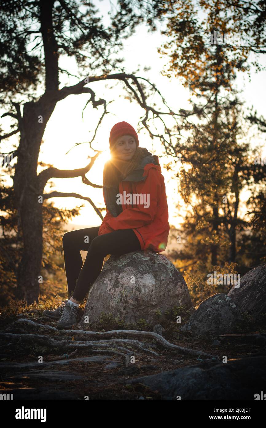 beau voyageur de brunette est assis au sommet d'une colline sur un rocher, se reposant après une forte montée. Coucher de soleil au sommet d'une montagne à Vuokatti, région de Kainuu Banque D'Images