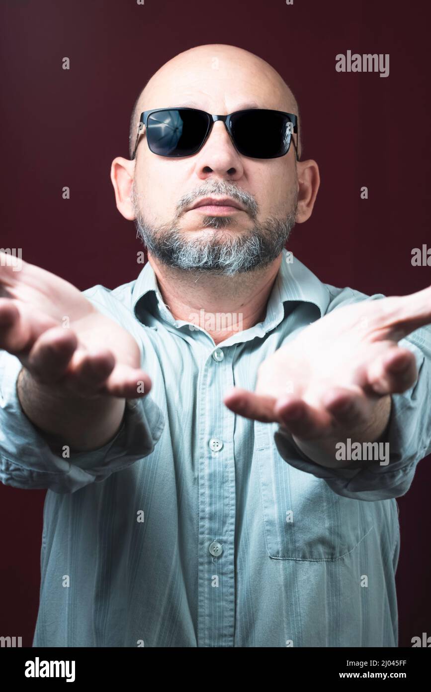 Portrait d'un homme barbu et chauve portant des lunettes sur un fond rouge foncé. Salvador, Bahia, Brésil. Banque D'Images