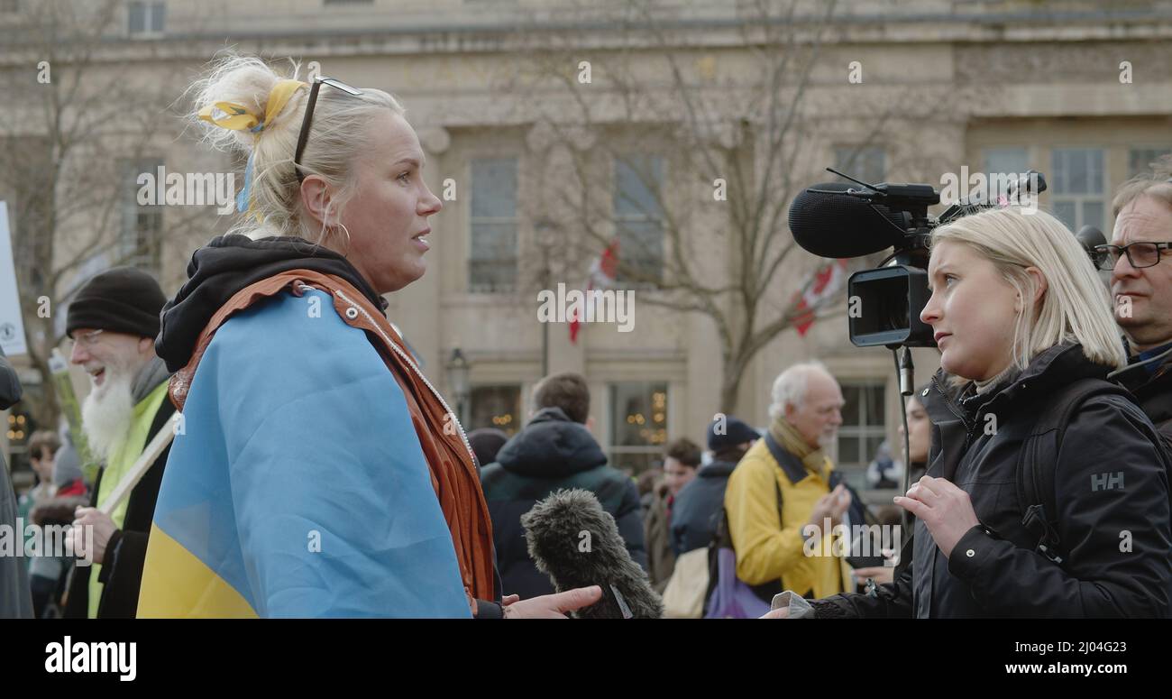 Londres, Royaume-Uni - 03 06 2022: Une femme ukrainienne proteste à Trafalgar Square, parlant à un journaliste, portant un drapeau bleu et jaune, pour soutenir l'Ukraine. Banque D'Images
