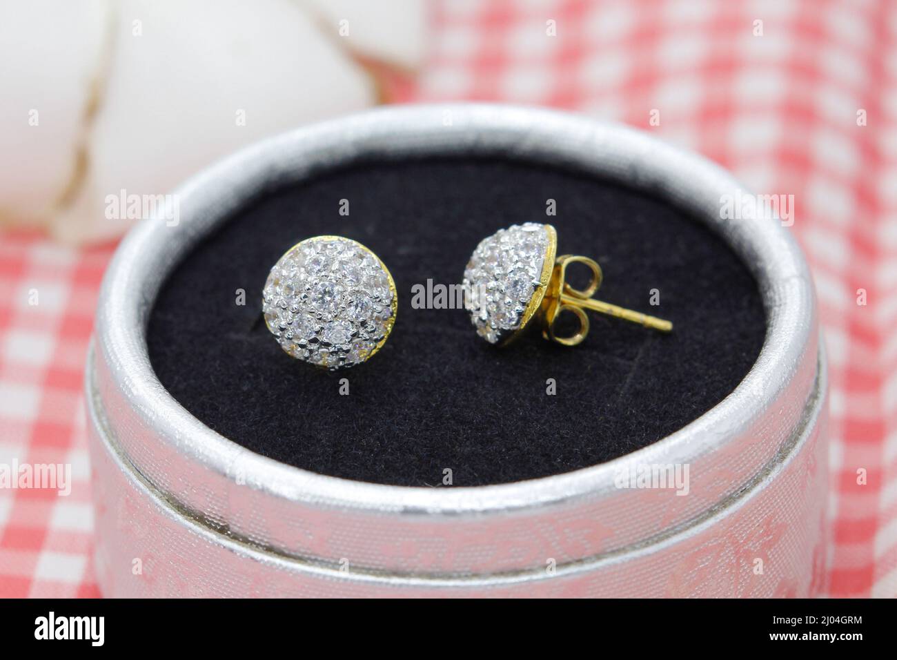 Belles boucles d'oreilles dorées décorées de diamants dans une boîte à bijoux sur fond de tissu écossais rouge Banque D'Images