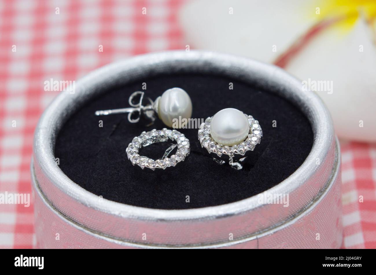 Boucles d'oreilles en perles authentiques Luxuly décorées de diamants dans une boîte à bijoux sur un tissu écossais rouge Banque D'Images