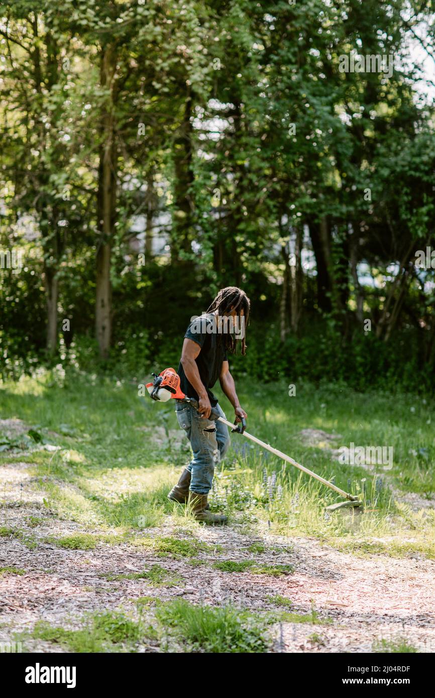 Homme noir utilisant un wacker de mauvaises herbes lors d'une journée d'été ensoleillée à Bridgeport, CT Banque D'Images