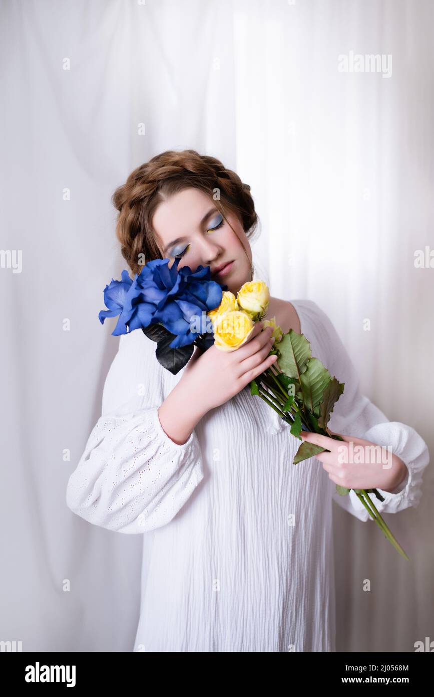 Portrait de la jeune fille ukrainienne de race blanche en robe blanche et fleurs sur fond blanc . Symbole de la couleur bleu jaune ukrainien. La dame calme est endormi. Concept - Arrêter la guerre en Ukraine. Banque D'Images