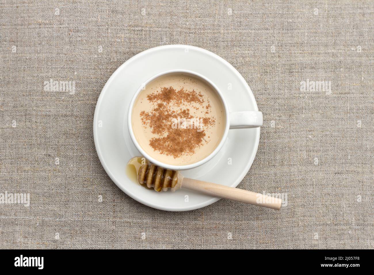 Thé chaud épicé avec du lait dans une tasse en porcelaine blanche avec miel et un panier de miel sur un fond textile Banque D'Images