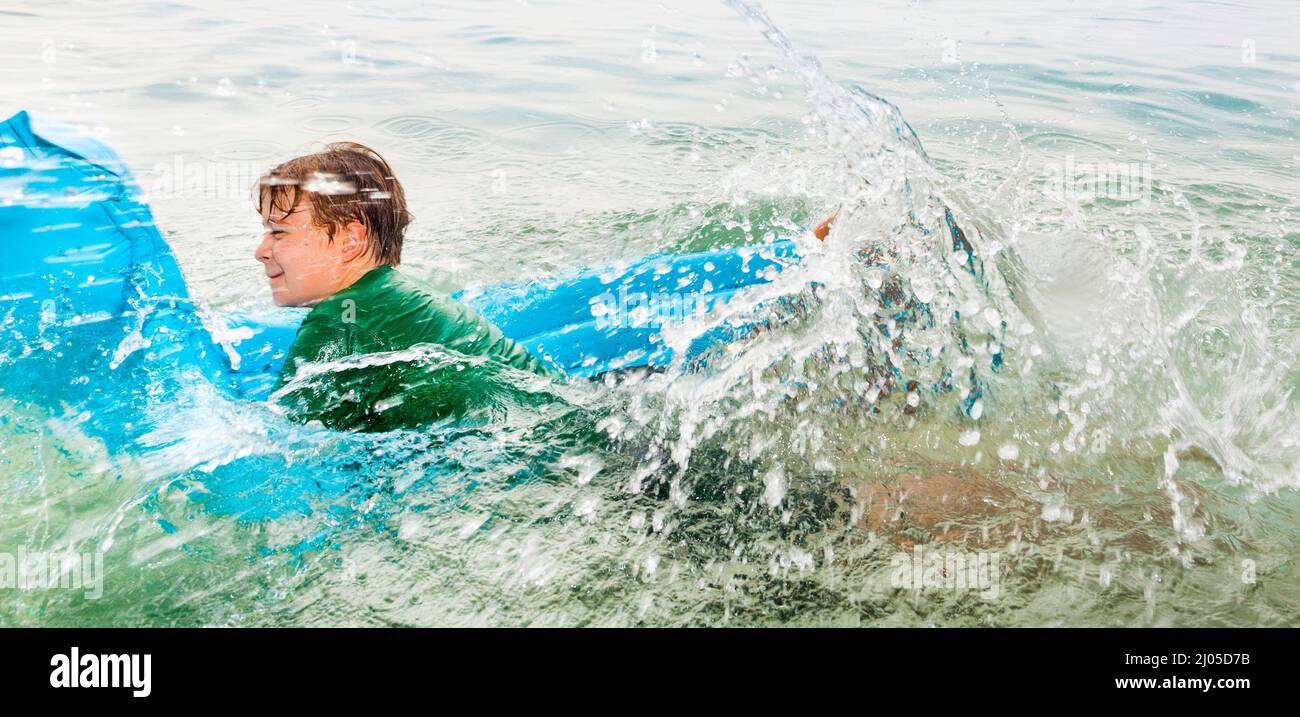 Jeune garçon s'amuse à sauter sur un matelas d'air dans l'océan Banque D'Images
