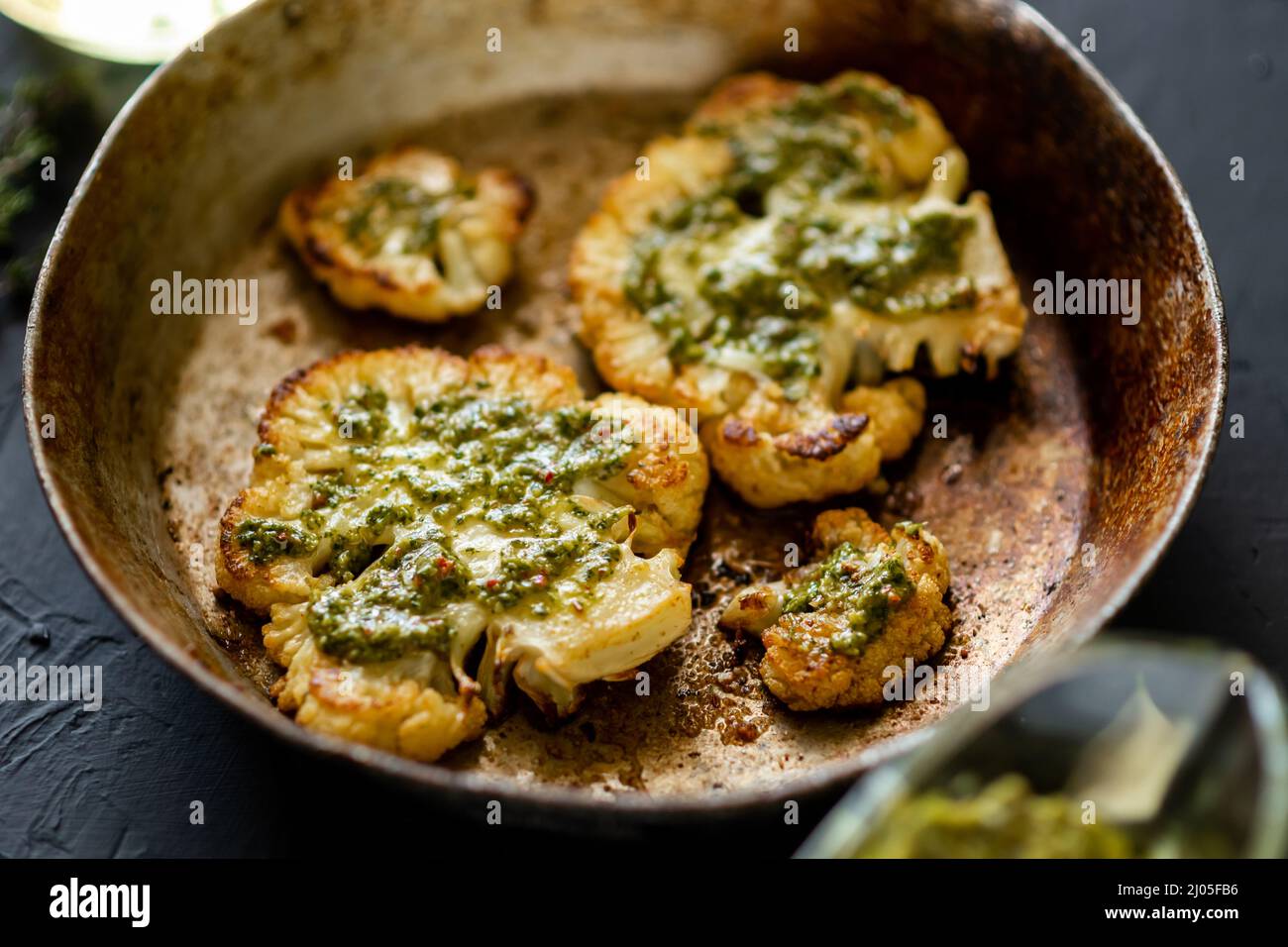 Le steak de chou-fleur aux épices se trouve dans une poêle. Huile d'olive,  sauce chimichurri, herbes, diverses épices côte à côte. Arrière-plan  sombre. Plats végétariens Photo Stock - Alamy