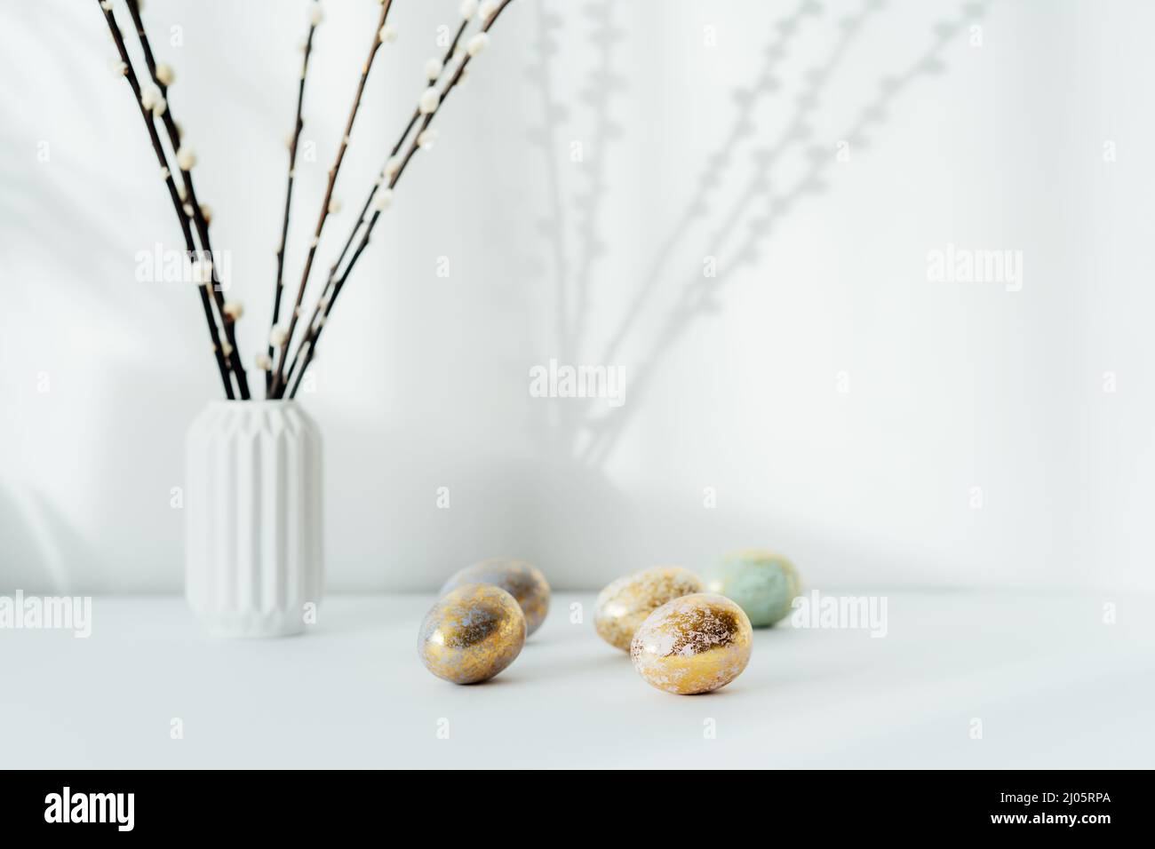 Intérieur de la maison avec décor de pâques. Branches de saule chatte dans un vase, oeufs dorés dans différents motifs sur la table blanche avec lumière et ombre backgroun Banque D'Images Intérieur de la maison avec décor de pâques. Branches de saule chatte dans un vase, oeufs dorés dans différents motifs sur la table blanche avec lumière et ombre backgroun Banque D'Images