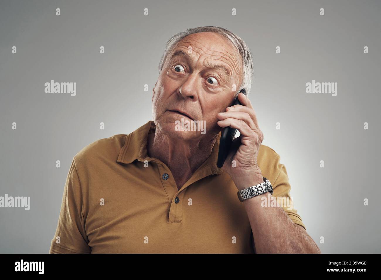 Dites-le de nouveau. Studio photo d'un homme âgé utilisant son téléphone portable sur fond gris. Banque D'Images