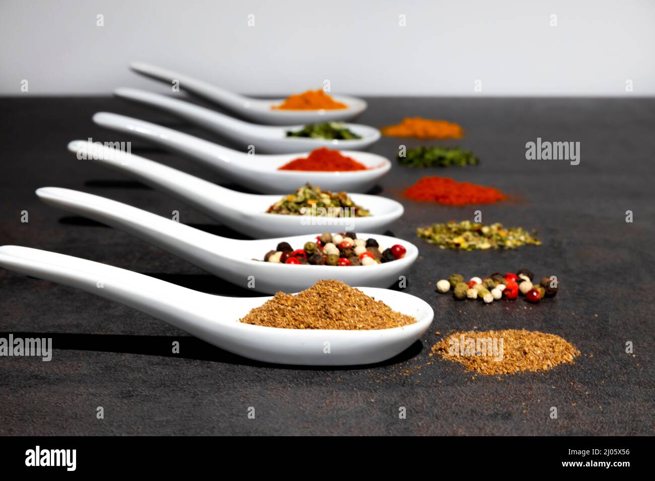 Herbes parfumées, épices de différentes variétés, en cuillères en céramique blanche, sur une table grise. Banque D'Images