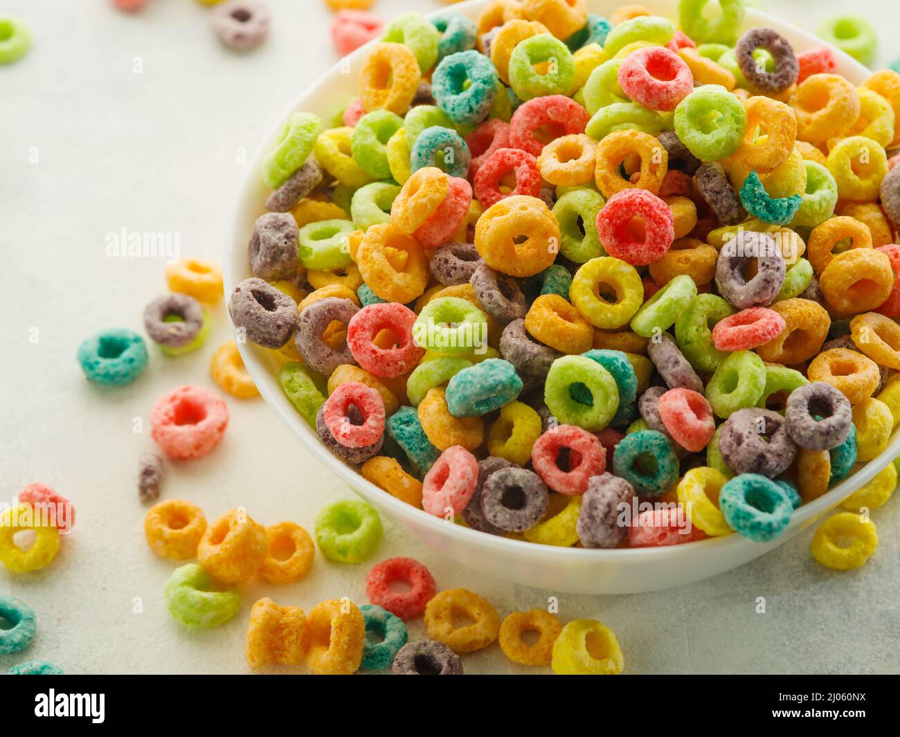 Prise de vue macro. Beaucoup de grains de fruits multi-couleurs anneaux  dans un bol et près d'elle sur un fond blanc. Céréales petits déjeuners  rapides, nourriture pour bébés, nourriture biologique, lui Photo