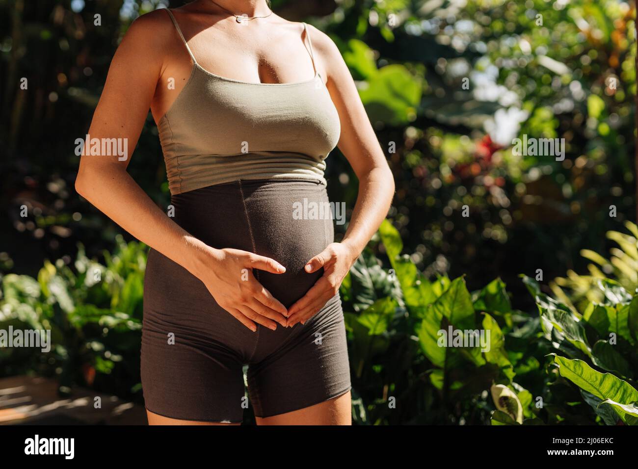 Les femmes enceintes font des poses de yoga à la maison avec le jardin sur l'arrière-plan et embrasser son ventre. Soleil d'été vibes Banque D'Images