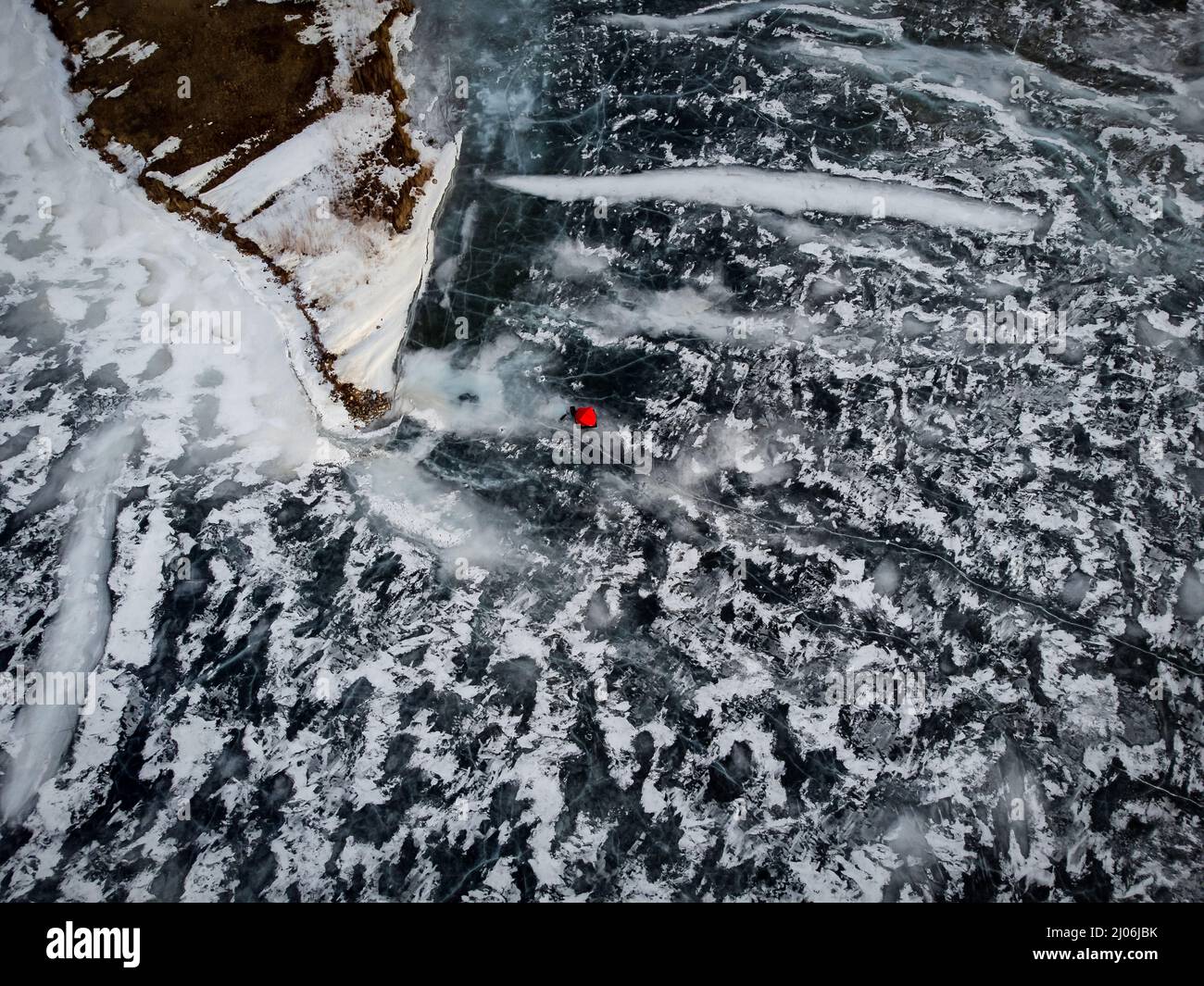 Vue aérienne en hauteur d'une tente de pêche sous la glace rouge sur un lac gelé avec de grandes fissures et une image satellite de l'île. Banque D'Images