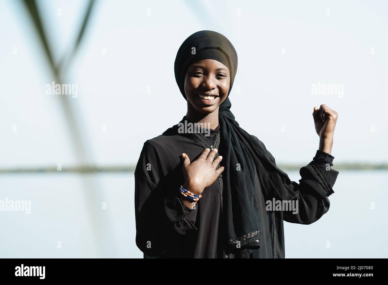 Vue de face d'une jeune fille africaine souriante, d'une main sur la poitrine et d'un poing levé, symbolisant la puissance, la confiance et l'estime de soi des femmes Banque D'Images