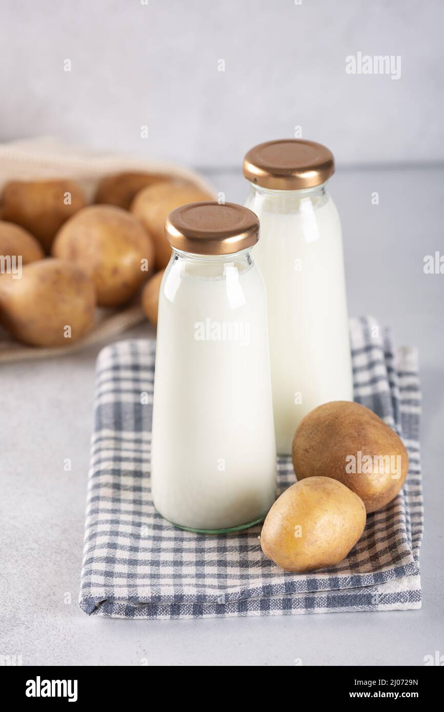 Bouteilles de lait à base de plantes végétaliennes. Boissons sans produits laitiers et tubercules de pommes de terre sur table grise Banque D'Images