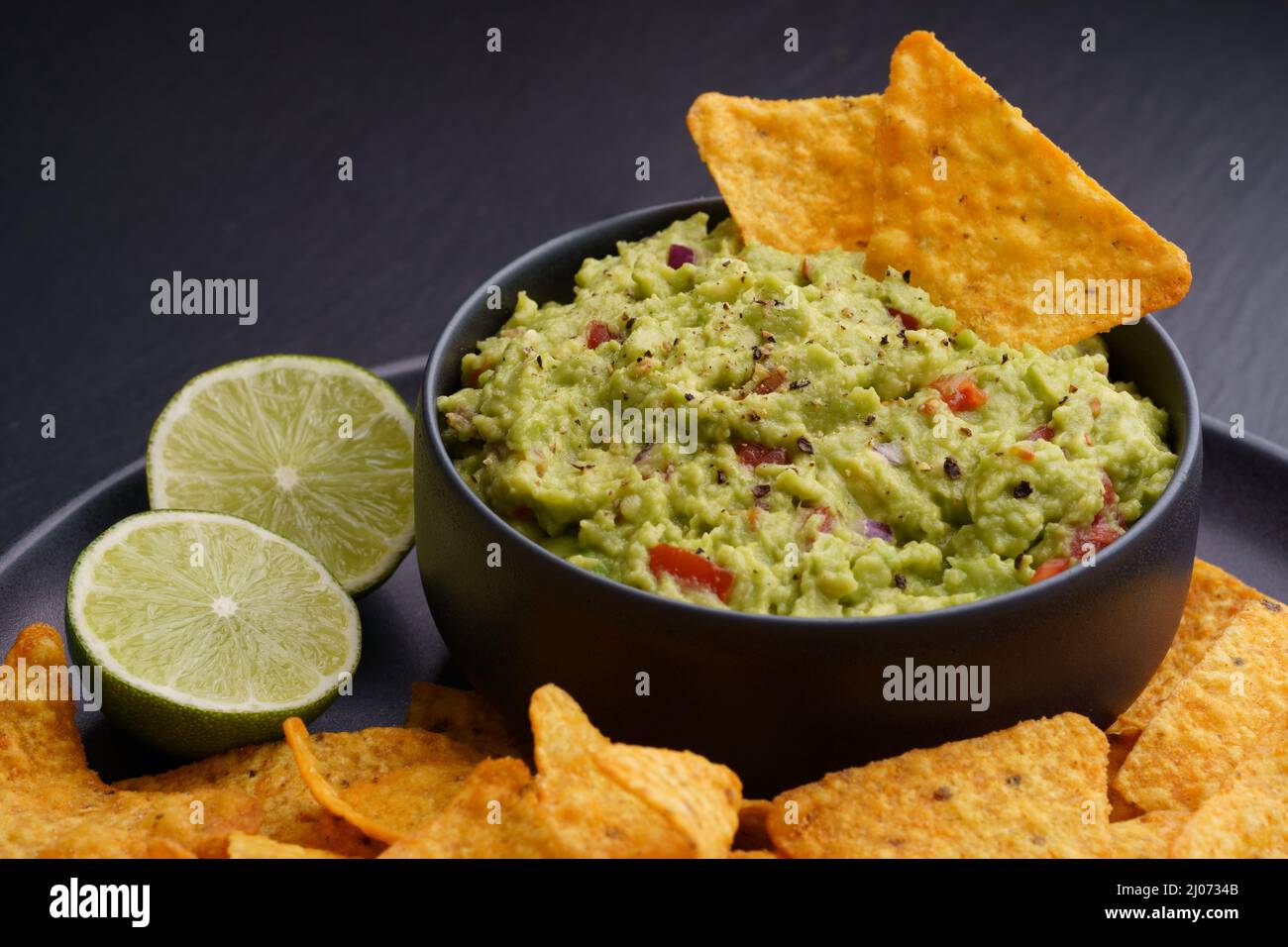 Trempez le guacamole avec des chips de tortilla ou des nachos et de la chaux sur fond noir Banque D'Images