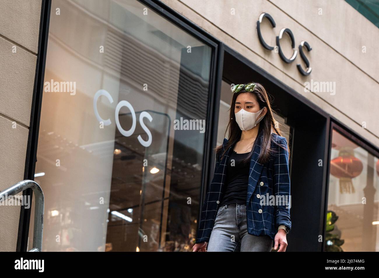 Une femme portant un masque chirurgical se promène près d'un magasin COS  dans le quartier central des affaires de Hong Kong. Selon l'analyse  économique du Gouvernement de Hong Kong, le secteur du