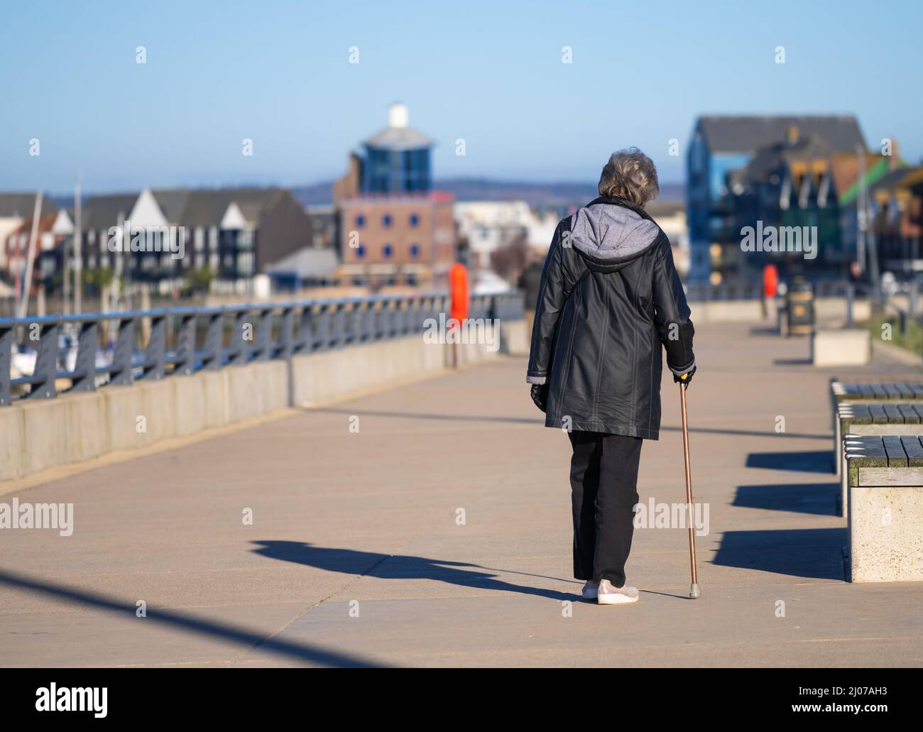 Femme âgée marchant avec un bâton de marche / aide à la marche le long d'un chemin de remorquage au bord de la rivière au Royaume-Uni. Banque D'Images