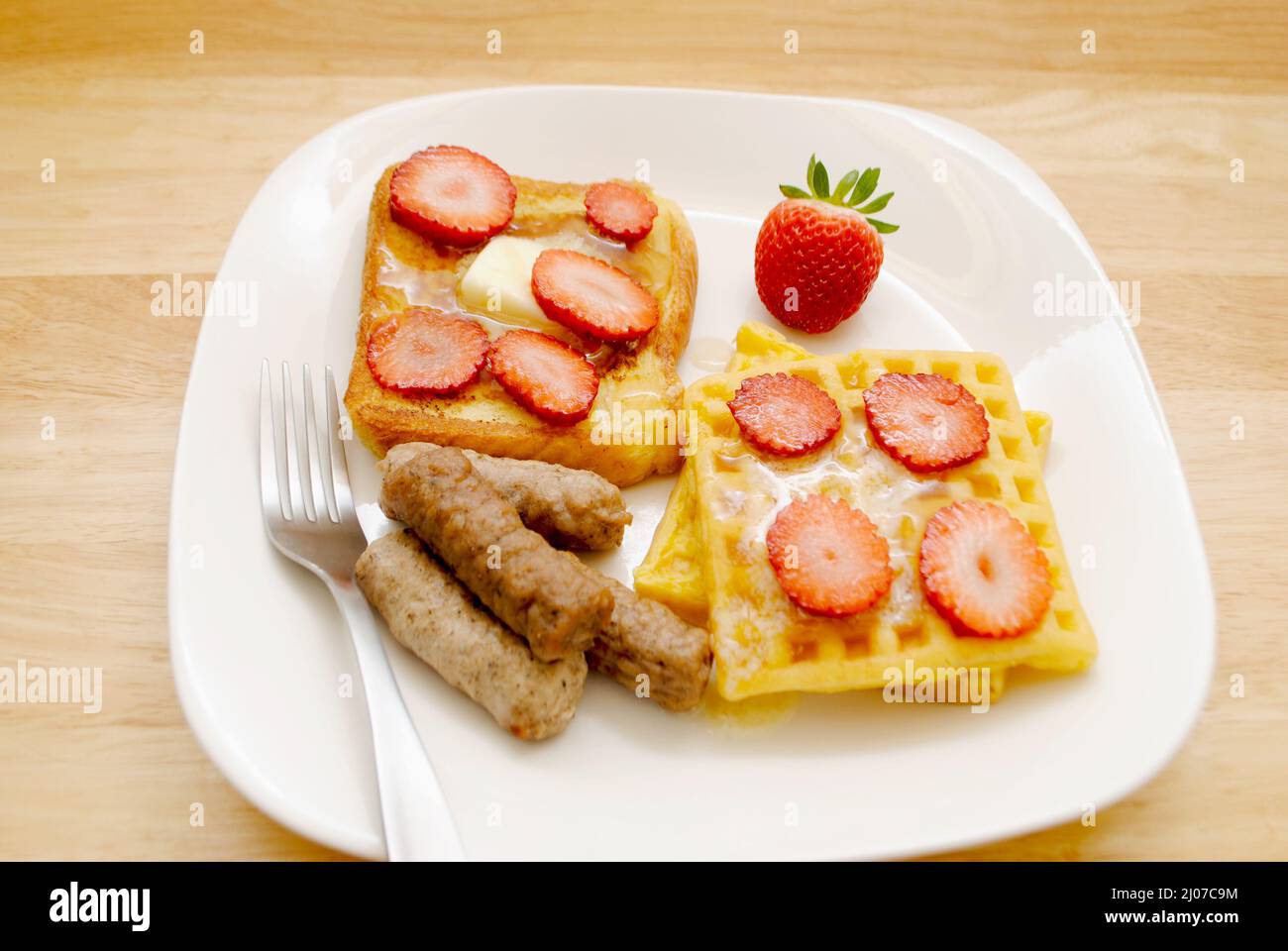 Pain grillé, gaufres avec sirop d'érable et fraises en tranches avec trois saucisses de porc sur une assiette blanche Banque D'Images
