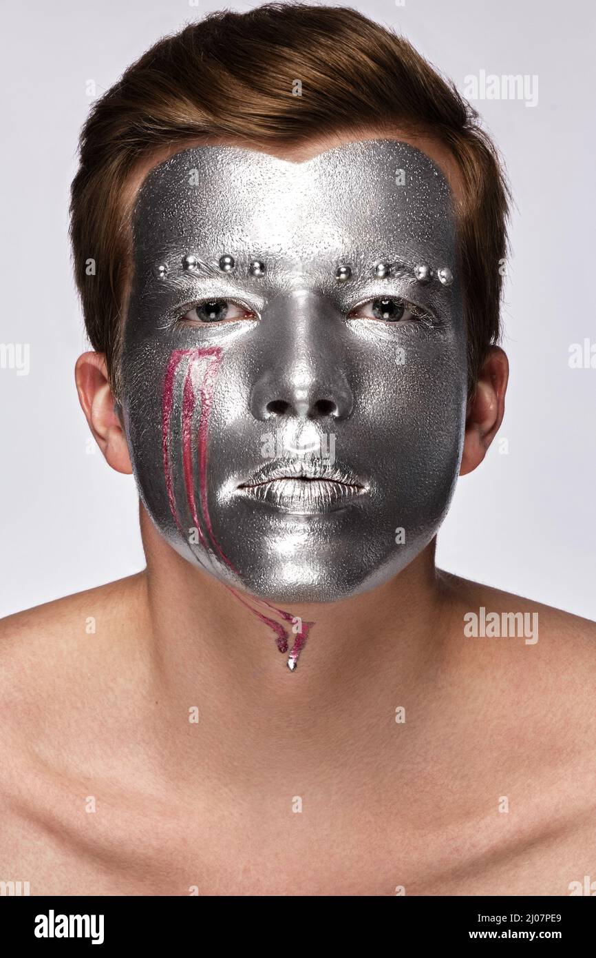 Jeune homme avec art créatif maquillage avec de la peinture argentée sur son visage. Banque D'Images