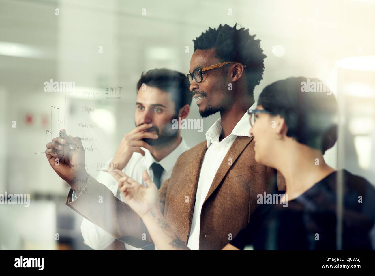 Faire tomber le plan une idée à la fois. Photo d'un groupe d'hommes d'affaires qui remue un brainstorming sur un mur de verre dans un bureau. Banque D'Images