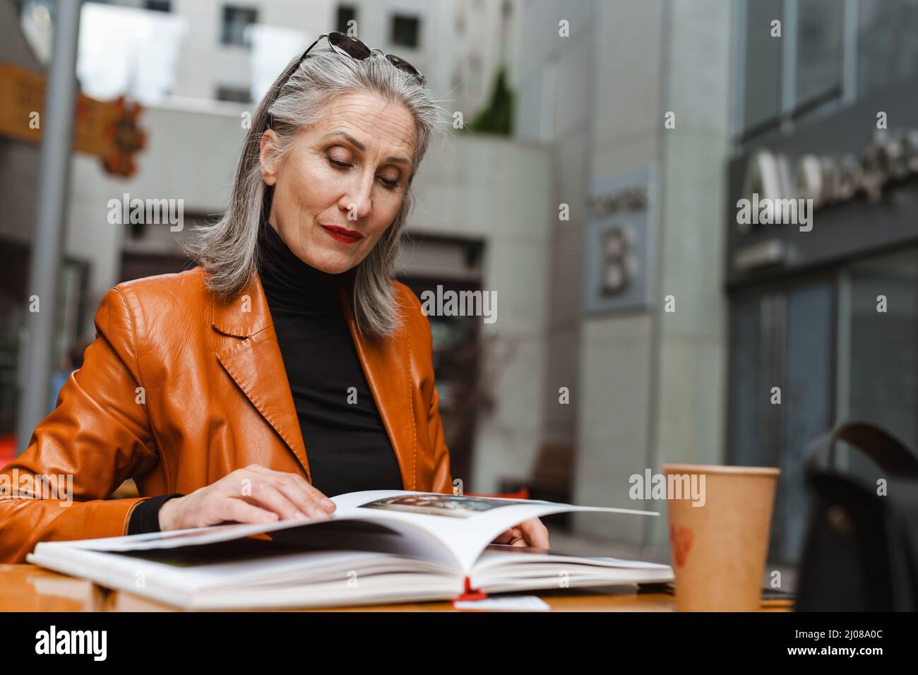 Femme âgée grise blanche lisant un livre tout en étant assise dans un café à l'extérieur Banque D'Images