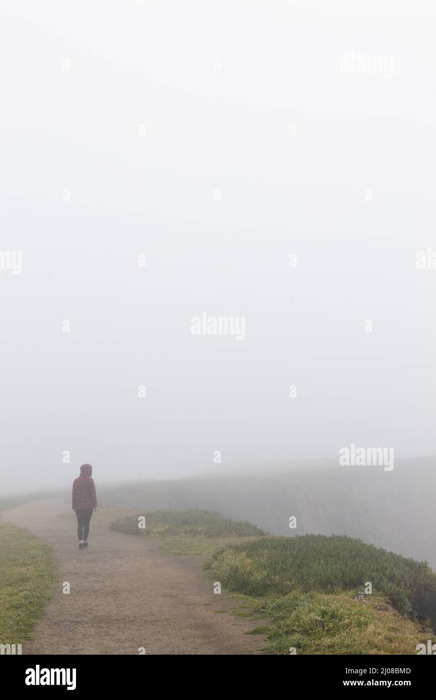 Une personne marchant le long d'un sentier sur le bord d'une falaise dans le brouillard. Banque D'Images