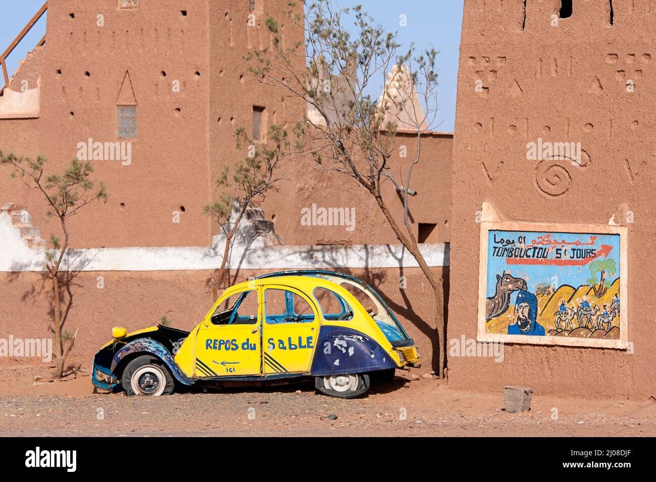 Panneau sur la maison de boue traditionnelle dans le sud du Maroc près de l'ancienne épave de voiture montrant des jours à dos de chameau à Tombouctou, à travers le désert du Sahara dans le centre du Maroc Banque D'Images