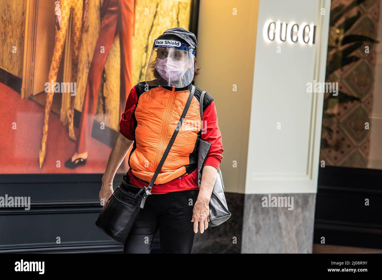 Une femme avec un masque de protection et un masque de protection marche près d'un magasin Gucci dans le quartier central des affaires de Hong Kong. Selon l'analyse économique du Gouvernement de Hong Kong, le secteur du commerce de détail est confronté à une pression énorme à court terme, la pandémie et les mesures de distanciation sociale qui y sont associées créent des défis pour une renaissance. Banque D'Images