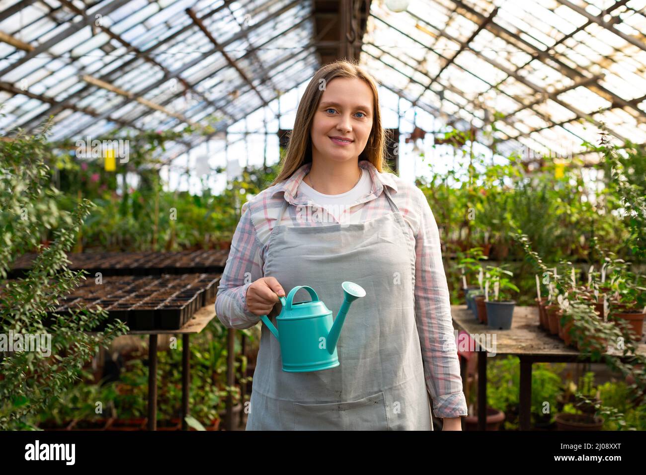 Portrait d'une jeune femme travaillant dans une serre. Elle regarde dans la caméra, sourit et tient un arrosoir dans ses mains. Banque D'Images