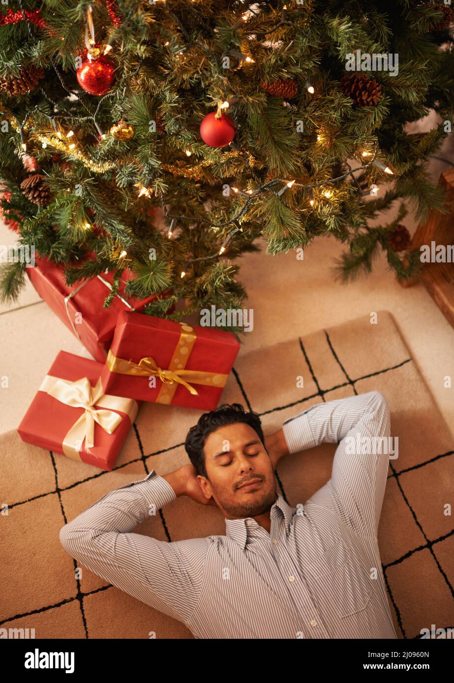 En attente du Père Noël. Photo d'un jeune homme qui se nappent sous l'arbre de noël. Banque D'Images