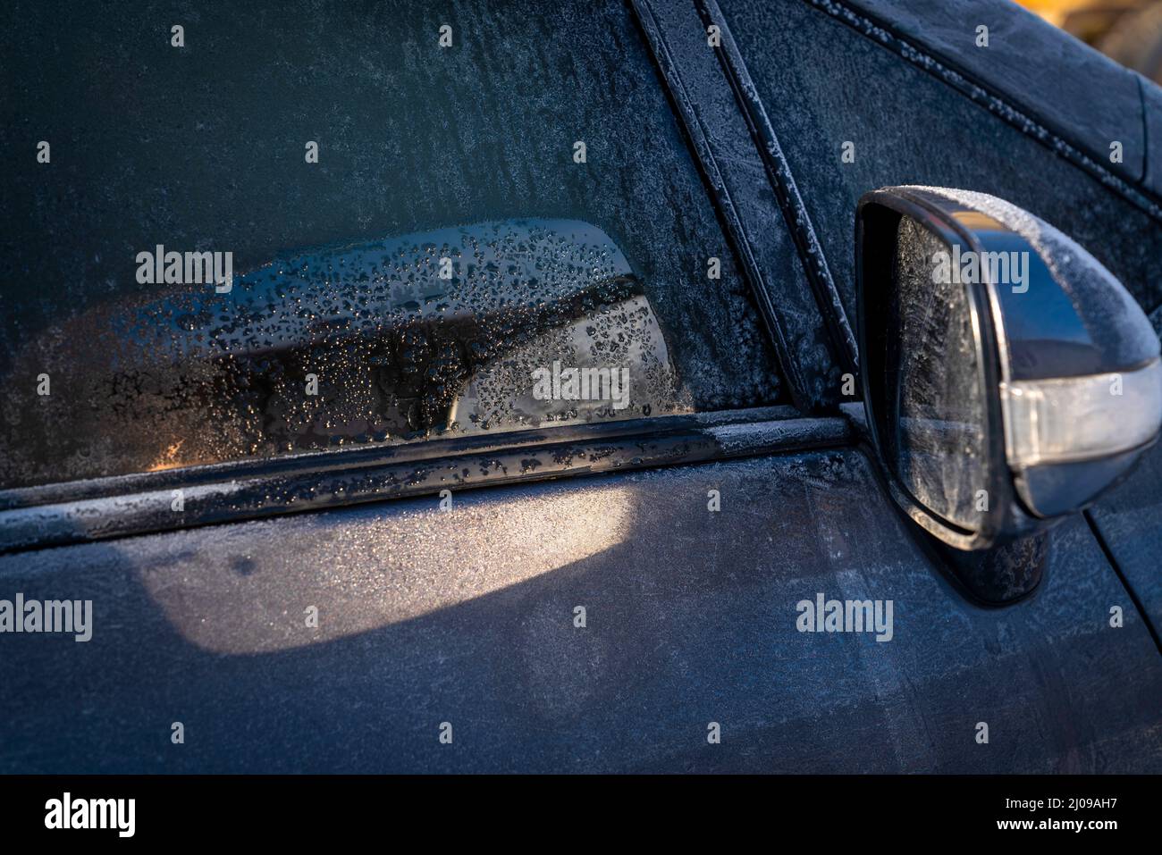 Le soleil frappant le miroir de la voiture lors d'un jour d'hiver dégèle le capot de la voiture réfléchi par le miroir. Banque D'Images