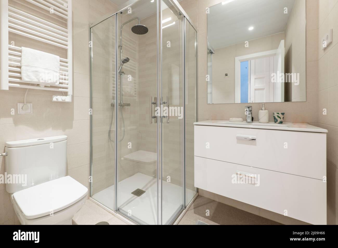 Salle de bains avec cabine de douche carrée avec cloison en verre, lavabo mural en porcelaine blanche, miroir rectangulaire et porte-serviette chauffant blanc Banque D'Images