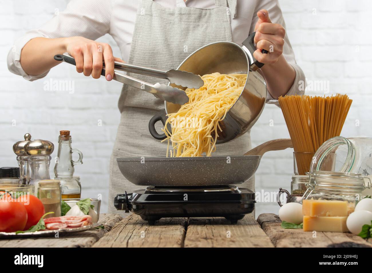 Chef dans des fours blancs uniformes spaghetti bouillis dans une poêle à frire. Arrière-plan de la cuisson des pâtes alla carbonara. Plat italien traditionnel sur fond blanc. Banque D'Images