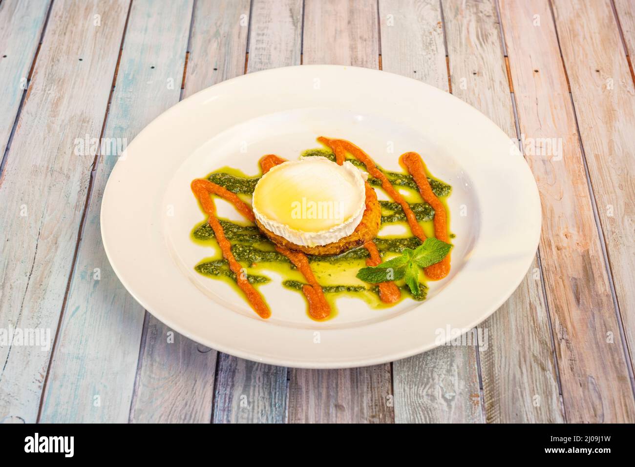 Tartine aux légumes avec fromage de chèvre, crème de carottes, sauce au pesto et huile d'olive sur une assiette blanche Banque D'Images