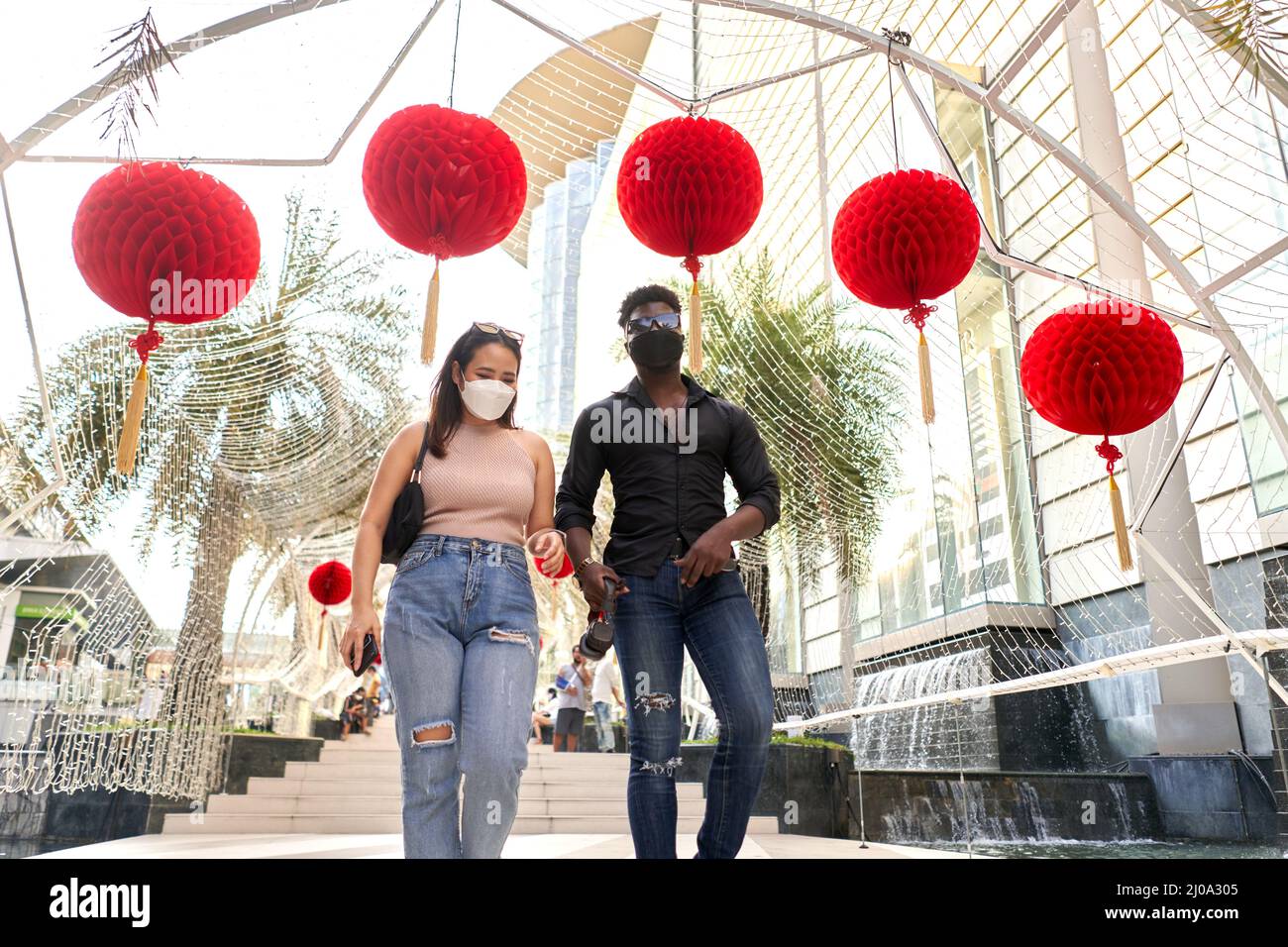 Deux amis multiraciaux avec masque marchant dans un centre commercial décoré de lanternes rouges Banque D'Images