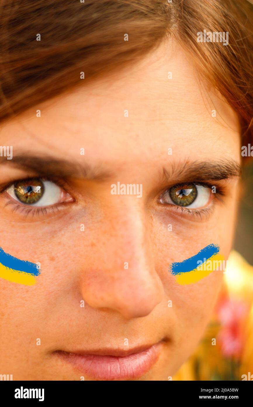 Drapeau ukrainien sur les joues. Gros plan d'une jeune femme de 20 ans, 25 ans. Yeux verts, cheveux bruns. Ensoleillé, coucher de soleil, aube. Le concept de Banque D'Images