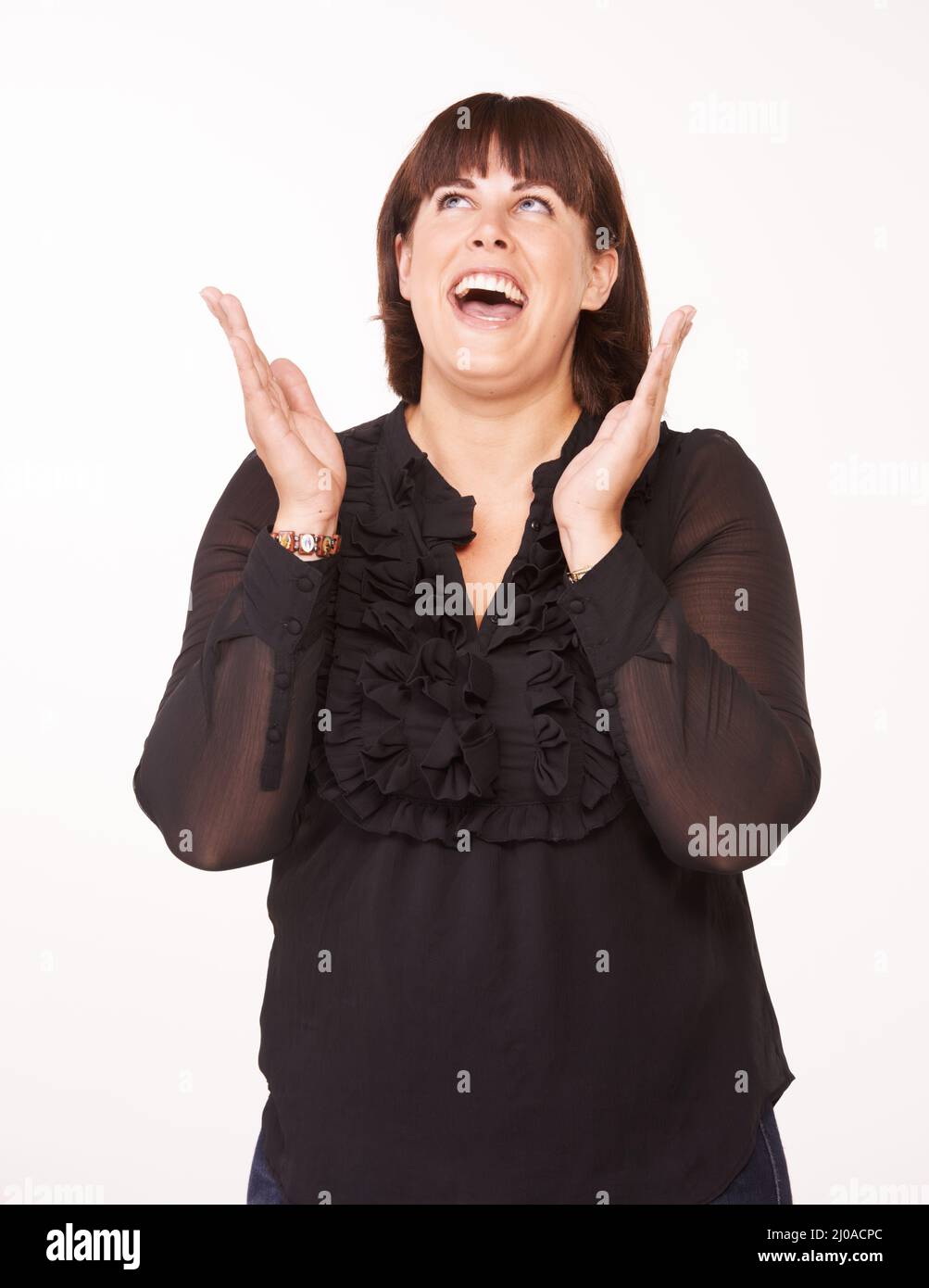 Ludique et amusant. Une jeune femme heureuse avec ses mains dans l'air tout en regardant vers le haut - fond blanc. Banque D'Images