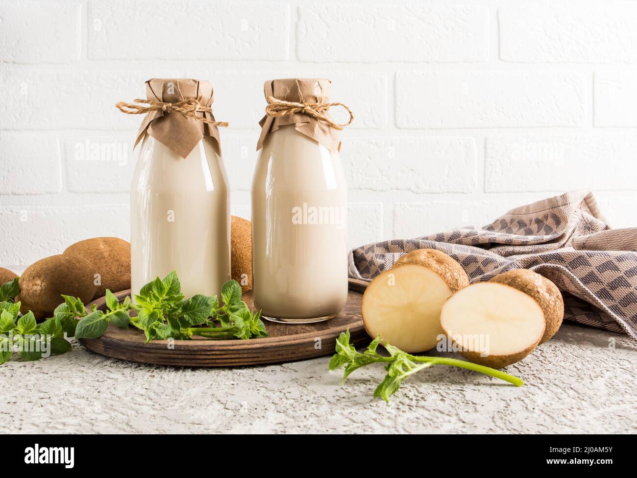 Le lait de légumes vegan des pommes de terre est une nouvelle tendance dans la consommation alimentaire. Deux bouteilles de lait en face d'un mur de briques blanches sur un plateau en bois Banque D'Images