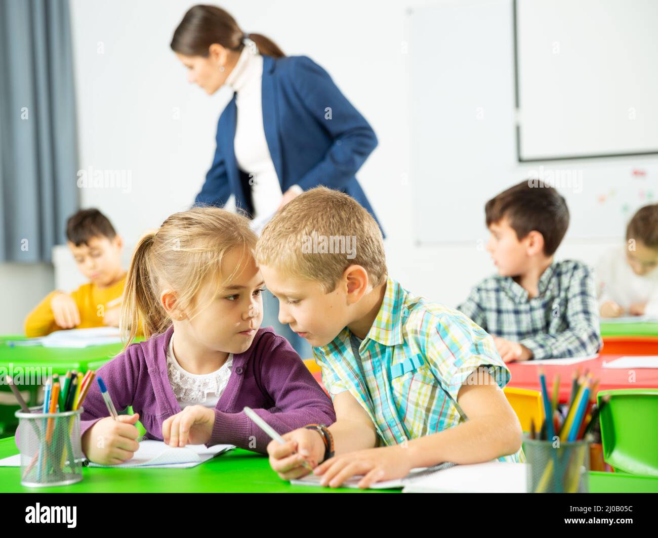 Les élèves heureux assis bavardant à leçon à l'école élémentaire Banque D'Images