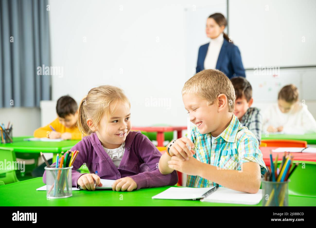 Les élèves heureux assis bavardant à leçon à l'école élémentaire Banque D'Images